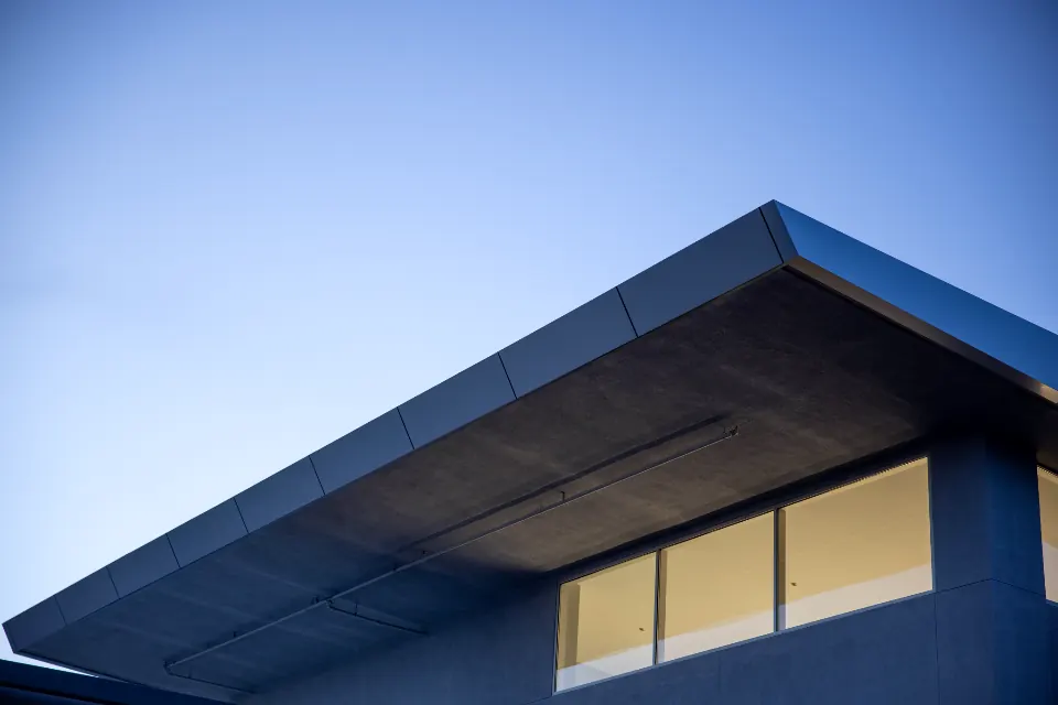 A modern house roofline and lit windows against a blue evening sky